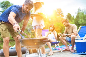 Man using bellows for preparing food in barbecue grill with friends on pier