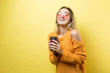 Glamor woman in glasses in an orange sweater with a drink of coffee on a yellow background	