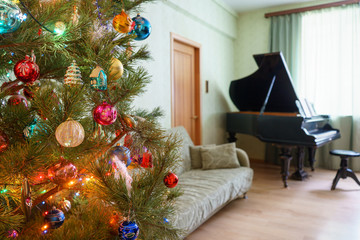 Beautiful festive decorated Christmas tree in living room interior with sofa, piano and window. Concept of new year holiday at cozy home