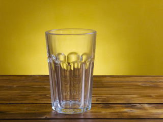 Empty glass on wooden table with yellow background