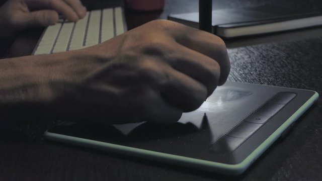 hands type on white keyboard and dark desk with graphic pen tablet and black notebook