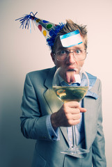 Disheveled office worker wearing a New Year's Eve party hat and a name tag stuck to his forehead licking an oversized wine glass at the holiday party