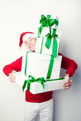 Smiling man in Santa hat peeking over a towering stack of Christmas presents with green satin ribbons