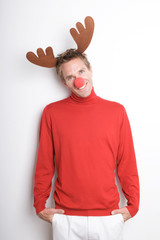 Young man with red nose and reindeer antlers standing looking at the camera in red turtleneck