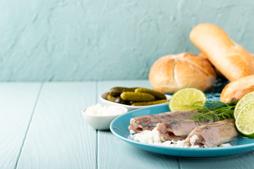Traditional dutch food freshly salted herring fish with onion called hollandse nieuwe on turquoise plate and wooden background. European food concept with copy space.