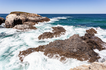 Ondas do mar a quebrar sobre rochas costeiras com espuma branca.
