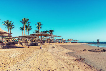 Beach with straw umbrellas and sunbeds. Egyptian resort in Sharm el Sheikh. Vacation concept.