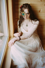 beautiful stylish bride in a fashionable dress posing in a hotel near the window. covered her eye with a peacock feather