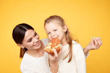 Mother and daughter eating pizza for lunch isolated over the yellow background