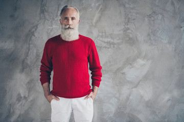 Photo of attractive aged guy holding hands in pockets self-confident wear red knitted pullover white trousers cool hipster santa clothes isolated grey color wall background