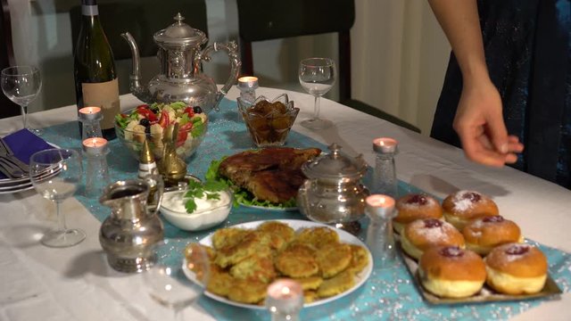 Festive family dinner. Traditional Hanukkah meal. On the table there is a jewish kosher symbolic fried food. Latkes, jelly-filled donuts, dairy produce, salad with cheese, chocolate Hanukkah gelt