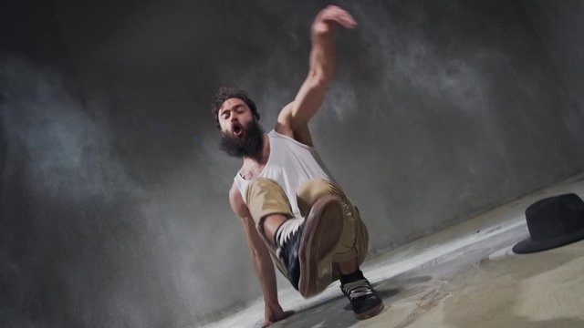 Beard guy a bboying style dancer does difficult tricks on the floor in a studio filled with flour on a black background.