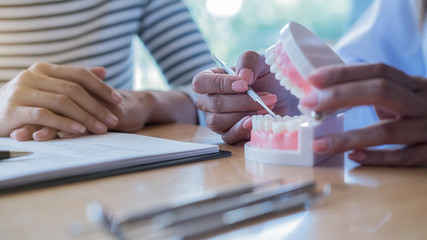 Dentist showing and explaining teeth disease treatment to patient using teeth model denture and...