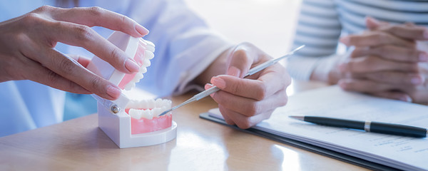 Dentist showing and explaining teeth disease treatment to patient using teeth model denture and...