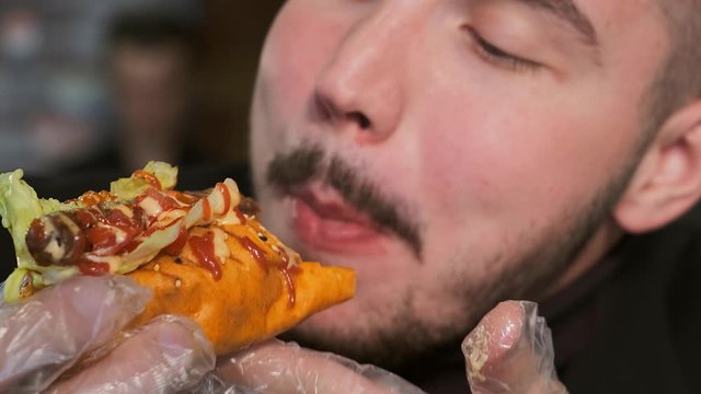 Extra large young man bites a hot dog in transparent gloves