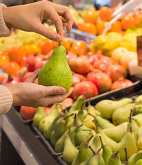 Female hand choosing pear in supermarket. Concept of healthy food, bio, vegetarian, diet.