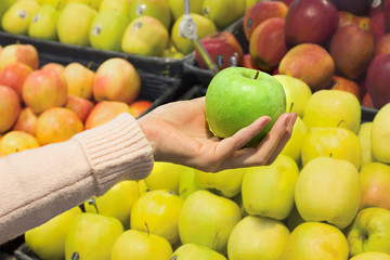 Female hand choosing apple in supermarket. Concept of healthy food, bio, vegetarian, diet.