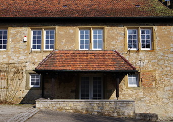 Fototapeta na wymiar Gepflegtes altes Haus mit Ziegel-Vordach und hellbrauner Steinfassade