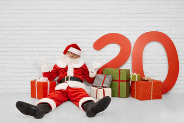 Santa Claus sitting on floor among gift boxes in studio