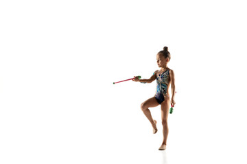 Little flexible girl isolated on white studio background. Little female model as a rhythmic gymnastics artist in bright leotard. Grace in motion, action and sport. Doing exercises with the maces.