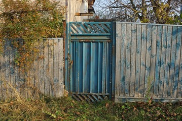 old blue metal door and gray wooden fence in green grass on a rural street