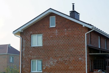  large brick brown house with windows under a tiled roof on a blue sky background