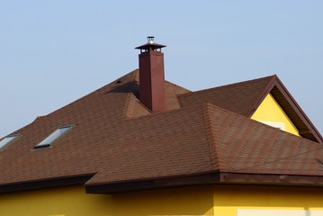 house roof with brown tiles and metal chimney against a blue sky