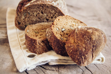 Brown fresh bread with seeds are cut into pieces on old wood background. Top view, copy space