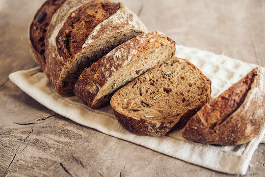 Brown fresh bread with seeds are cut into pieces on old wood background. Top view, copy space