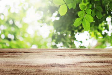 Wooden table with beautiful sunlight and blurred green leaves nature in the garden bokeh background.