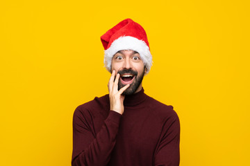 Man with christmas hat over isolated yellow background with surprise and shocked facial expression