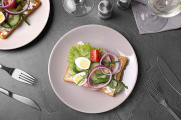 Tasty sandwich with ham and quail eggs served on grey table, flat lay