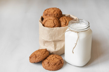Milk in a glass jar and oatmeal cookies in a paper bag on a white table background. Copy, empty space for text