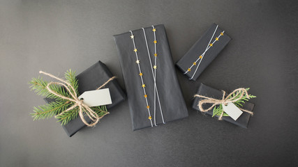 Top view on stylish Christmas New Year or birthday gifts in black paper decorated with gold stars and fir branches.