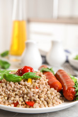 Tasty buckwheat porridge with sausages and vegetables on light grey marble table indoors, closeup. Space for text