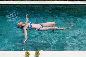 The happy slender young woman lies on a water surface in the pool and has a rest