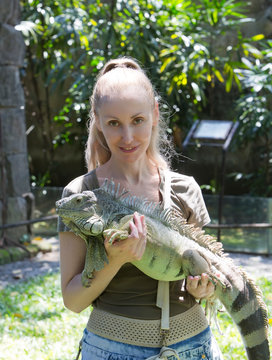 The young woman holds iguana on hands..