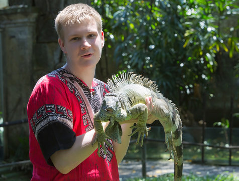 The young man, the teenager holds an iguana on hands