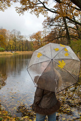 woman under a transparent umbrella on autumn day on the river shore..