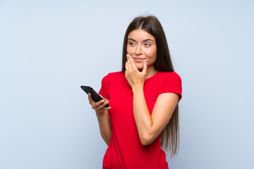 Naklejka premium Brunette young woman with a mobile phone over isolated blue wall thinking an idea