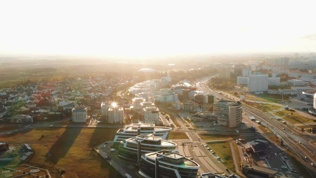 Drone flying above modern city buildings and parks panorama in Minsk, Belarus during sunrise on clear autumn day.