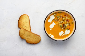 Healthy organic pumpkin cream soup with cream, croutons, seeds and basil on a light wooden background