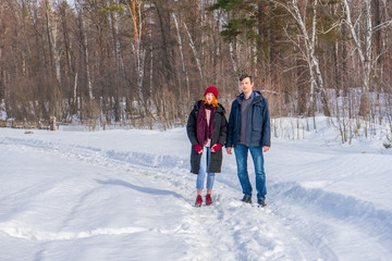Handsome man and attractive young woman walking along snowy country road in sunny day. Beautiful look, male and female fashion, winter outfit. Winter holidays, weekend at countryside concept