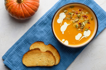 Healthy organic pumpkin cream soup with cream, croutons, seeds and basil on a light wooden background