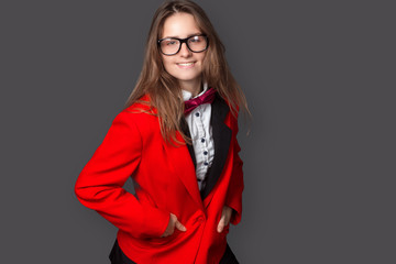 girl in white shirt, black vest and red jacket with Burgundy bow tie and classic black pants office style and glasses smile on gray background