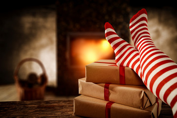 Woman legs with white and red christmas socks.Burred fireplace in home interior.Xmas gifts with...