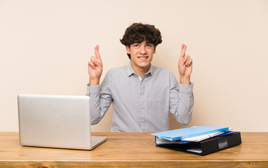 Young student man with a laptop with fingers crossing and wishing the best