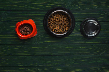 top view of bowls with pet food in row on green wooden surface