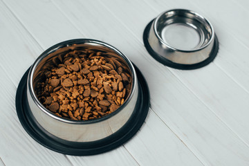metal bowl with pet food and empty bowl on white wooden surface
