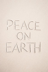 Peace On Earth holiday message handwritten on smooth sand beach